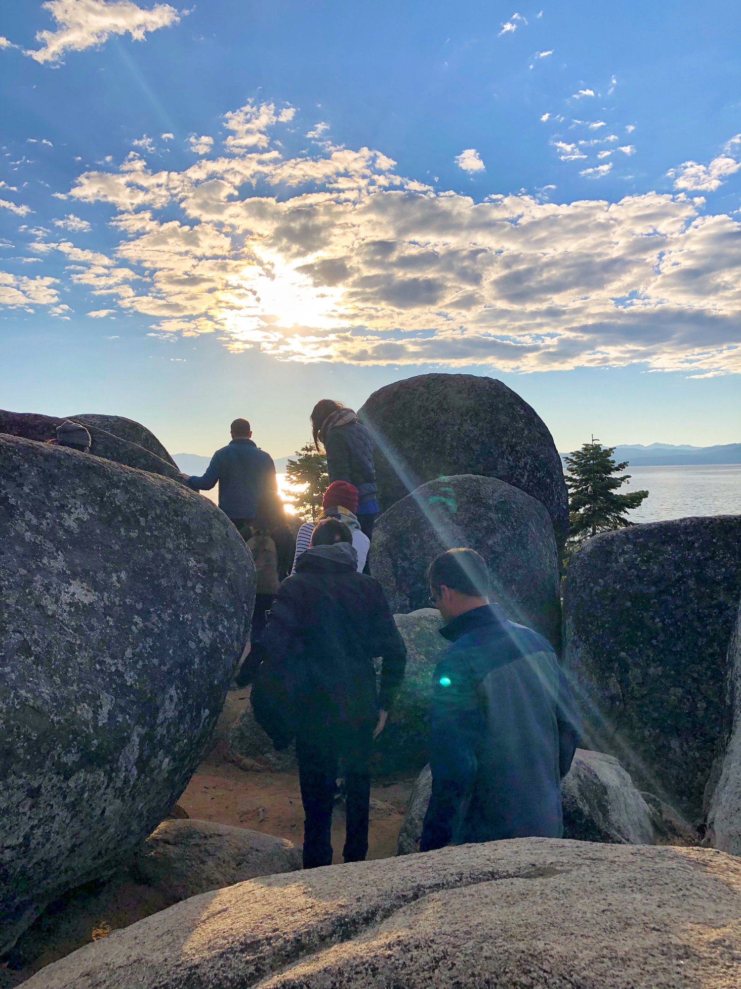 People helping each other over rocks toward a sunset